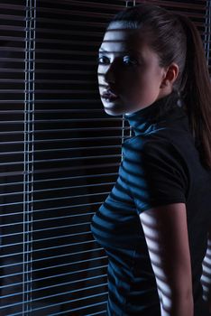 Sexy woman in black dress with jalousie looking through the window with jalousie