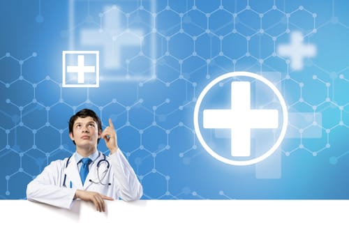 Young handsome doctor holding white blank banner. Place your text