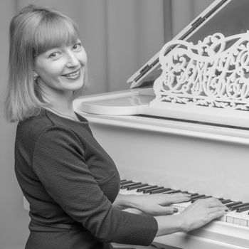 Beautiful young woman near a white grand piano. The concept of musical education, creative development of personality.Black and white photo. Retro style.