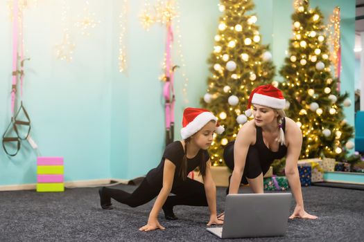 Beautiful flexible young woman and a girl go in for sports at Christmas near a decorated Christmas tree, sports and holiday. High quality photo.