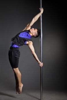 Young strong pole dance man over black background with flashes