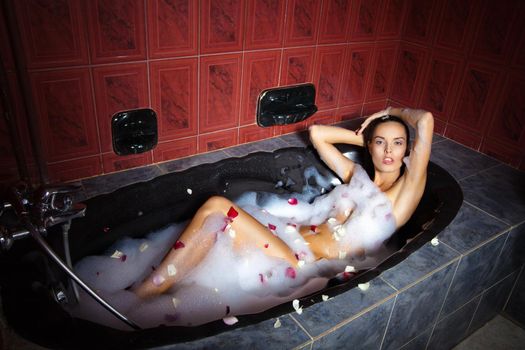 Beautiful woman relaxing in a black bathtub in red bathroom