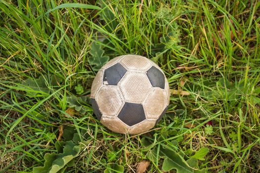 Old Soccer ball on the green grass, top view.