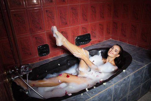 Beautiful woman relaxing in a black bathtub in red bathroom