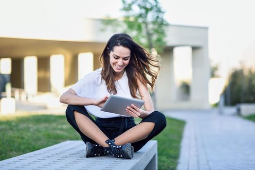 Young woman using digital tablet sitting outdoors in urban background.