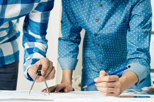 Architect measuring with compass divider on construction drawing on desk. Professional designers discussing architecture project. Teamwork and project brainstorming. Industrial engineering company.