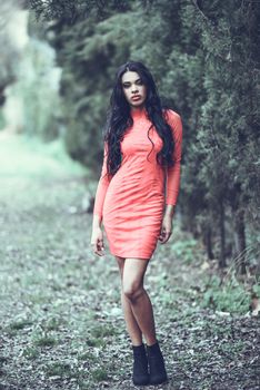 Portrait of hispanic young woman wearing orange dress in urban park