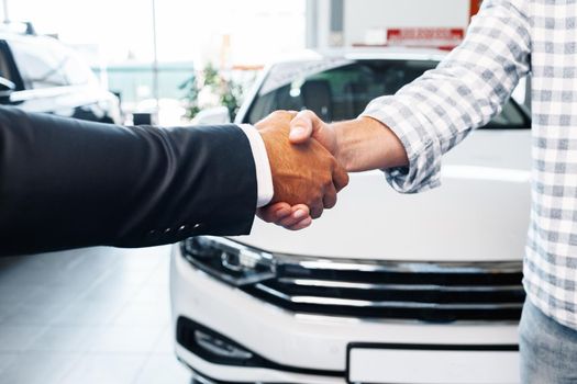 Customer shaking hands with professional car dealer at automobile dealership close up