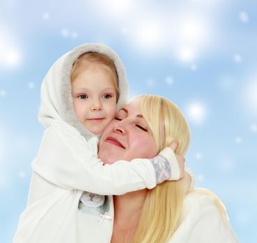 Cute little girl tenderly embraces the neck of his beloved mother.Blue Christmas festive background with white snowflakes.