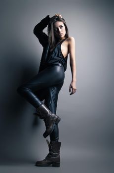 Fashion model wearing leather pants and jacket posing on grey background