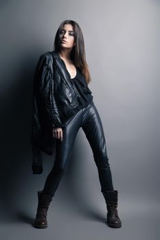 Fashion model wearing leather pants and jacket posing on grey background