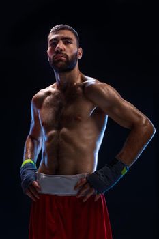 Handsome athletic guy in a red shorts on a black background. The boxer is fetching his breath after practicing hooks and blows. Professional fighter. Studio shot