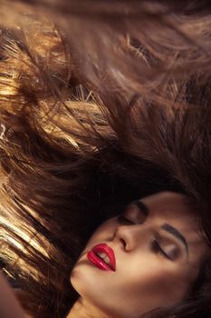 A beauty shot of a young woman with red lips and flowing hair over dark background