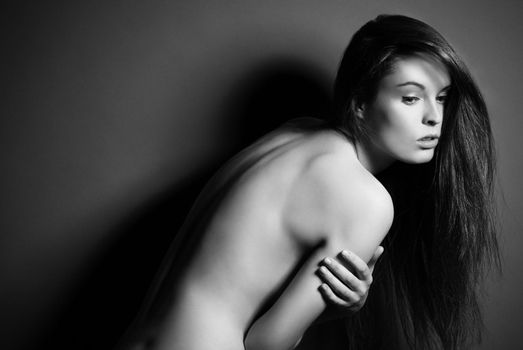 Portrait of beautyful naked posing brunette woman with long straight hair on dark grey background