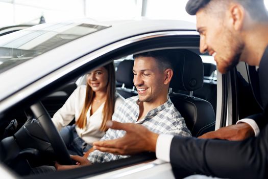 Young couple choosing a car at the dealership with manager helping them