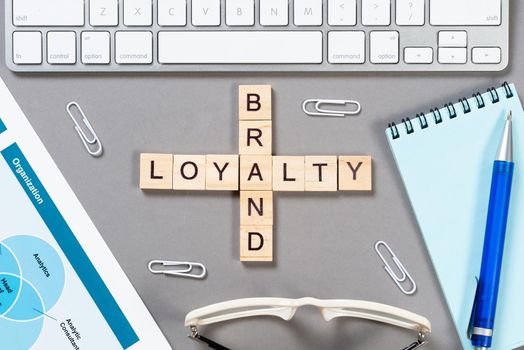 Brand loyalty concept with words from cubes. Still life of office workplace with crossword. Flat lay grey surface with computer keyboard and calculator. Strategy planning and business management.