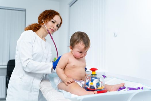 Pediatrician doctor concept. Children medical care. One year old baby girl examined by female pediatrician in clinic office. Child visiting doctor for health check-up. Doctor examine little patient.