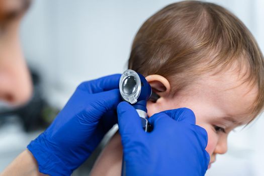 Red-haired female doctor examines little child for less than a year in a modern clinic. Pediatrician during examination baby in the hospital. Childrens healthcare. Diagnostics and treatment for kid.