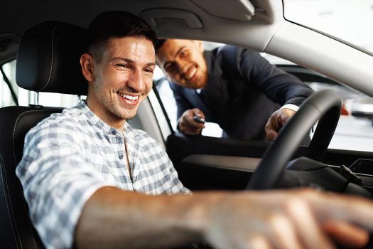 Cheerful young man customer buys a new car in a car dealership