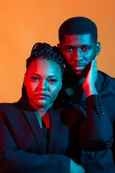 Portrait of young african american couple in love posing at studio dressed in classic clothes. Neon light