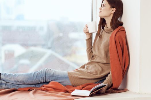 woman with a book near the window with a cup of coffee. High quality photo