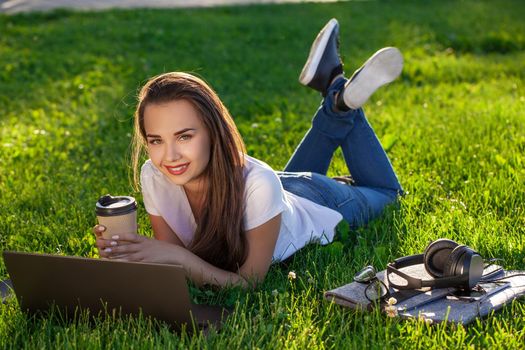 Young woman using laptop in the park lying on the green grass. Modern lifestyle, information technology or online shopping concept