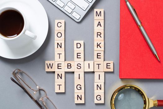 Web marketing concept with words from cubes. Still life of office workplace with crossword. Flat lay grey surface with pc keyboard and cup of coffee. New strategy planning and workflow optimization.