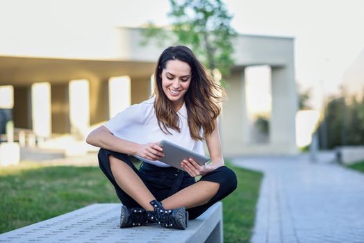 Young woman using digital tablet sitting outdoors in urban background.