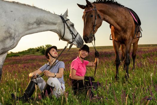 Two woman and two horses outdoor in summer happy sunset together nature. Taking care of animals, love and friendship concept.