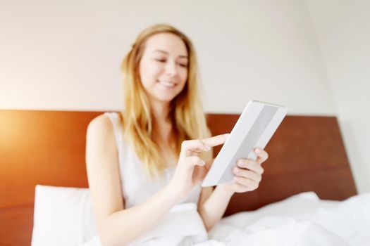 focus on tablet, rejoicing young european woman working happy remotely at white bed. concept of new technologies, advertising sales and remote freelance