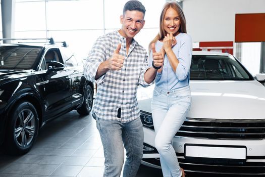 Cherrful young couple at the dealership buying a new car indoors