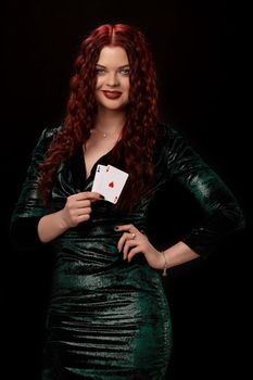 Charming redheaded woman whith a curly hair and red lips, posing with a playing cards in her hands and smiling, on black background Win casino poker slots