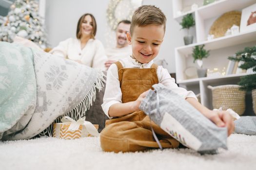 Happy little boy unwrapping his xmas gifts at home, portrait