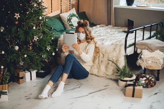 caucasian woman with medical mask on her face wishes happy new year to her family with a tablet