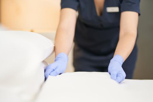 Close up of female chambermaid in protective gloves making bed in hotel room. Hotel service concept