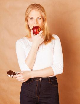 young beauty blond teenage girl eating chocolate smiling, choice between sweet and red apple