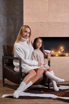 Beautiful mother woman in white sweater hugs her little daughter. Cheerful playful mood and love inside the family. Cozy home environment.