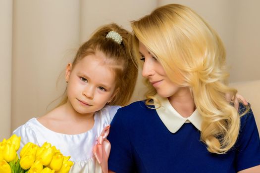 A beautiful young mother and little daughter near a bouquet of tulips, which her daughter gave to her mother for the holiday. The concept of women's holiday, family values.