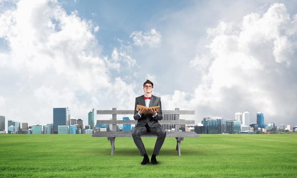 Young student sits on a wooden bench with a book