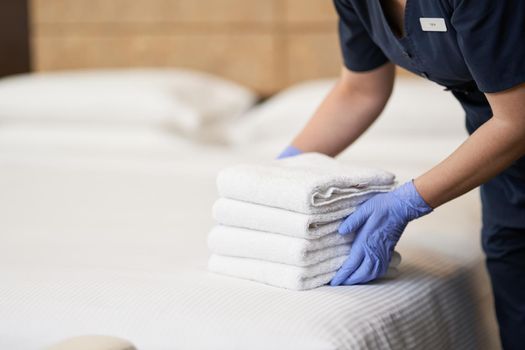Cropped photo of maid in uniform putting towels on the bed in hotel apartment. Hotel service concept