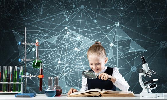 Little girl sitting at desk with magnifier and open book. Research and education in school. Happy schoolgirl in school wear carefully studying book. Clever girl reading book with magnifying glass.