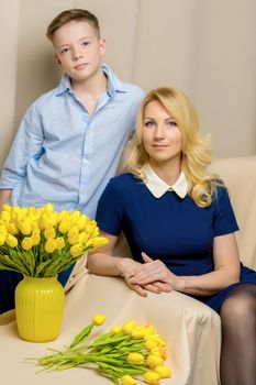 A beautiful young mother and son of school age near a bouquet of tulips, which the son gave his mother for a holiday. The concept of women's holiday, family values.