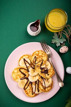 Healthy breakfast with fresh hot pancakes with bananas and chocolate on green background, top view.