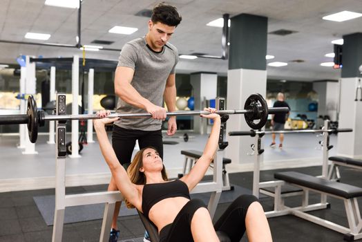 Personal trainer helping a young woman lift weights while working out in a gym