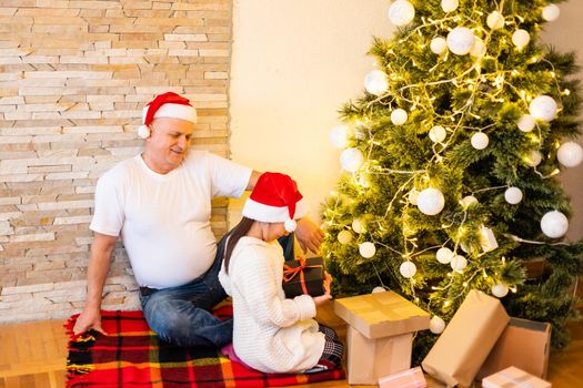 family, holidays, generation and people concept - smiling girl with grandfather decorating christmas tree at home