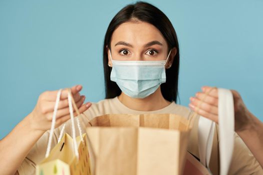 Waist up of surprised woman holding shopping bags and looking at camera. Copy space. Quarantine, coronavirus concept