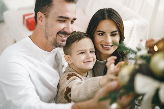 Family of 3 decorating a Christmas tree at home, close up