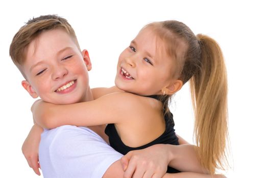 Charming little girl hugging a tall boy with blond hair. A romantic couple is happy with the joint time brought. A happy sister hugs her brother. The concept is a happy childhood. Isolated on white background.