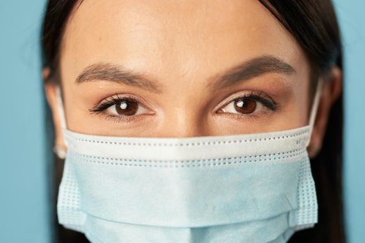 Close up of beautiful lady making mask protection from virus epidemic, isolated on blue background. Copy space. Quarantine, coronavirus concept