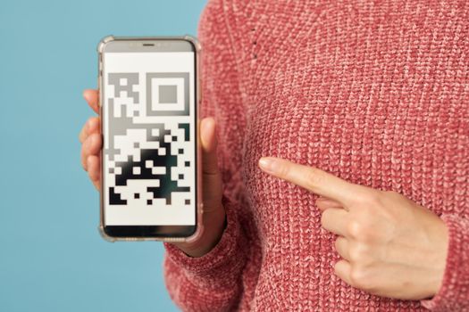Cropped photo of woman holding smartphone and pointing her finger at screen with barcode on it. Shopping concept